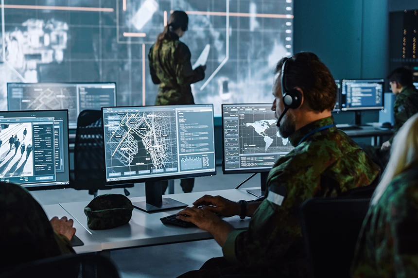 Two individuals in a high-tech control room monitoring global data, with one person facing large screens displaying maps and another person seated at a desk with multiple monitors.