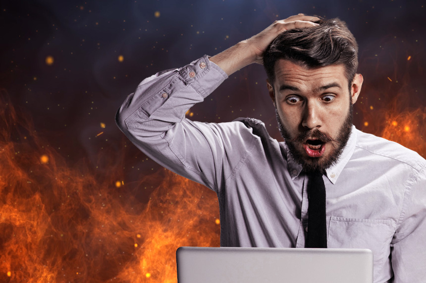 man with shocked face looking at laptop with fire in background
