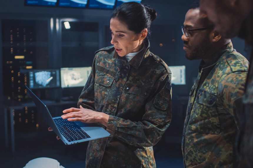 three military personnel gathered around laptop