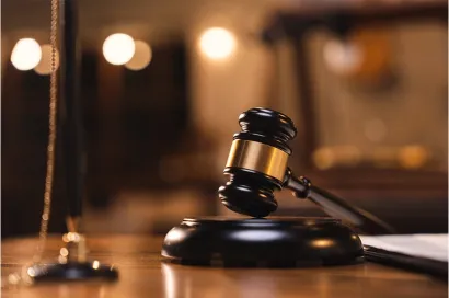 A close-up image of a gavel on a wooden block in a courtroom, with a blurred background.