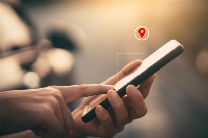 Image: a person holds a phone and an illustrated pin above the phone points to a location