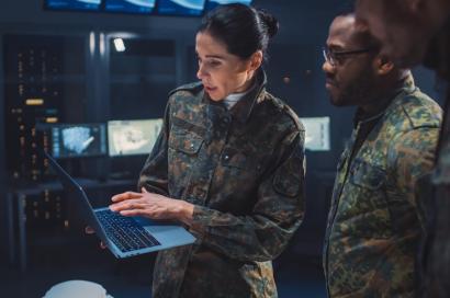 three military personnel gathered around laptop